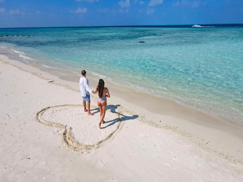 couple standing on beach with a heart in the sand solo travel while in a relationship