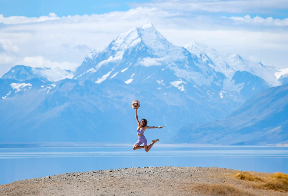 female jumping in the air in front of a mountain landscape in new zealand