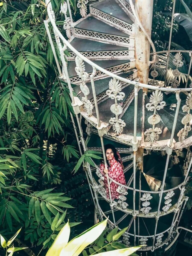 spiral stairwell surrounded by green plants and a female in a tulip dress standing on the stairs in kew gardens, london.