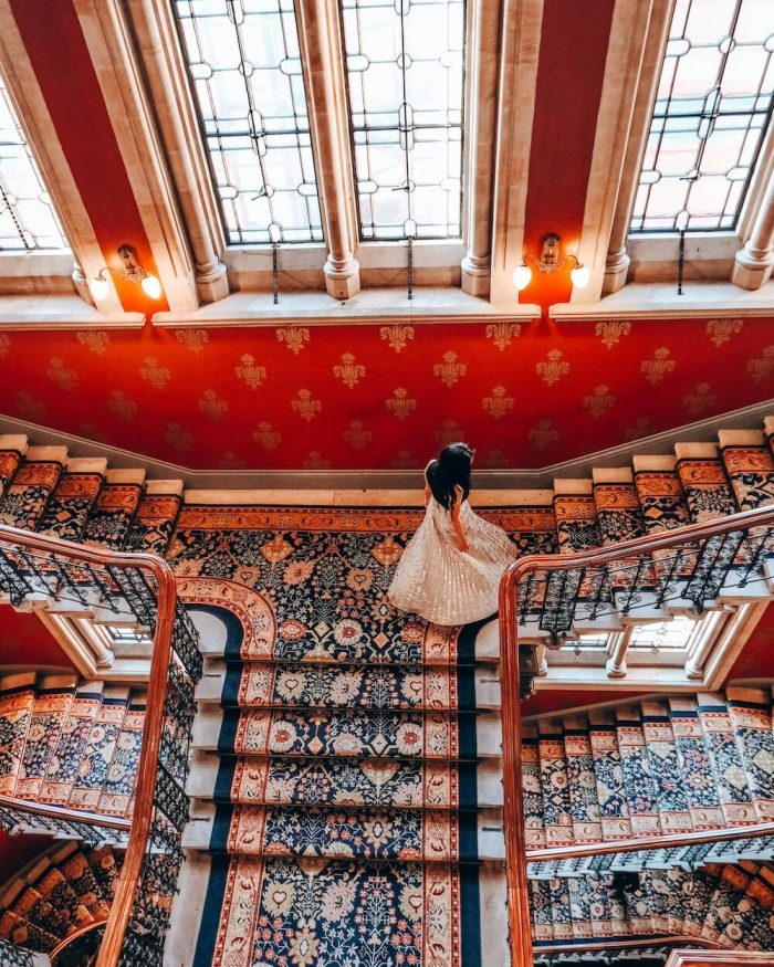 female in a gold skirt standing for an instagram photo of stairwell at st. pancrass renaissance hotel in london king's cross