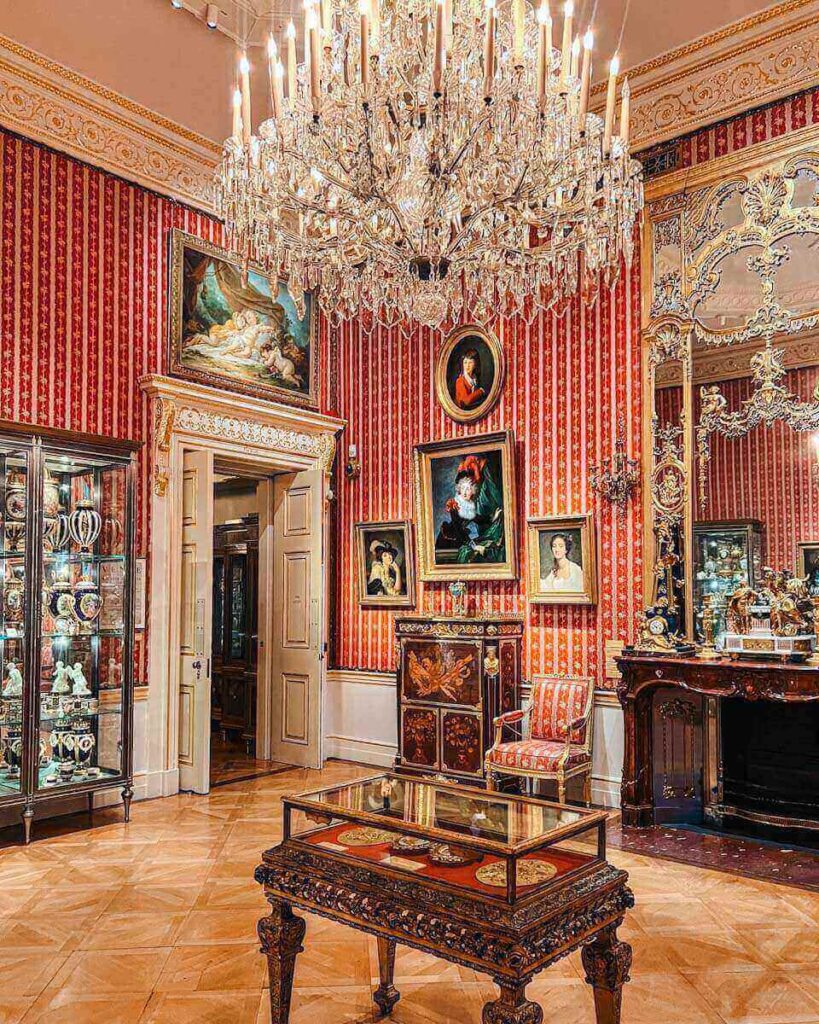 red ornate room with a glass chandelier at the Wallace collection in London