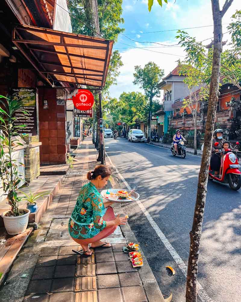 woman setting an offering in canggu bali and scooter drivers on the road