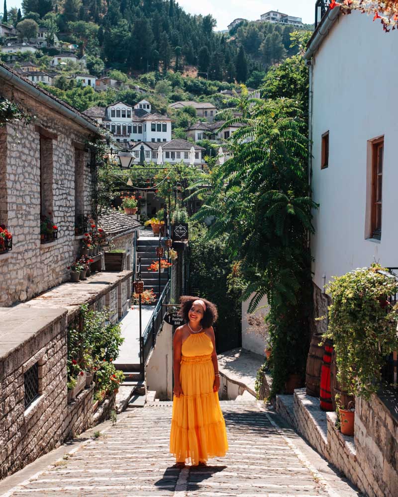 female in a yellow dress on a street in Gjirokastër with stone houses in the background